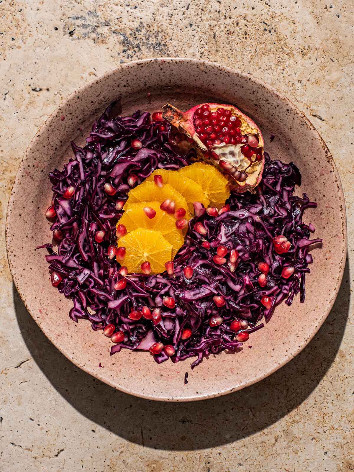 A shallow bowl of red cabbage salad with orange and pomegranate.