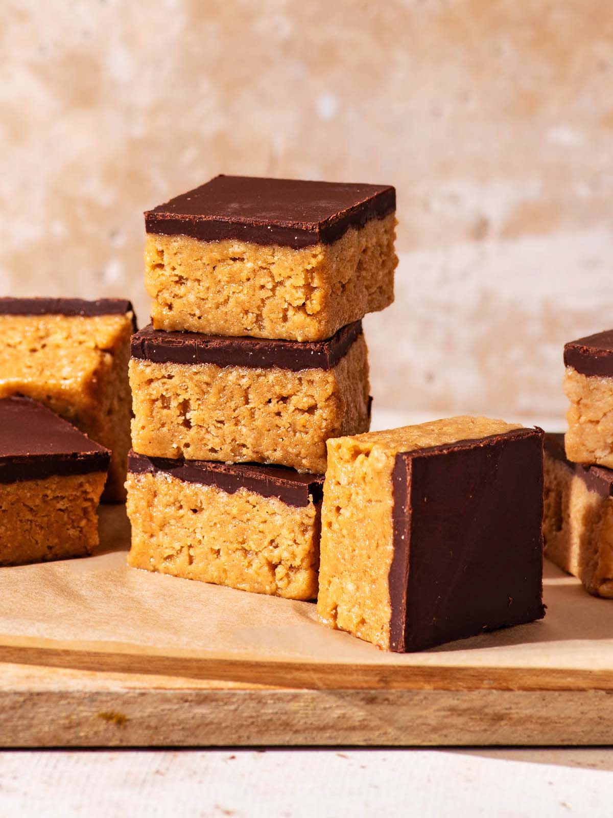 Several chocolate-topped peanut butter bars stacked and piled on a small cutting board.