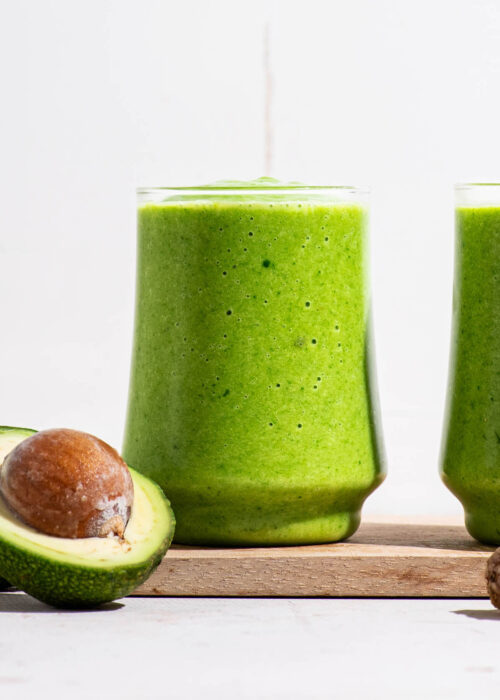 Green smoothie in two glasses with a halved avocado.