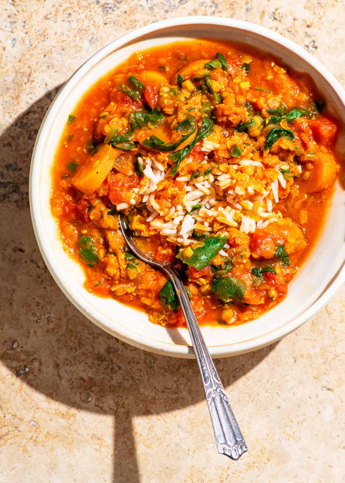 Bowl of red lentil soup in bright direct light on a stone background.