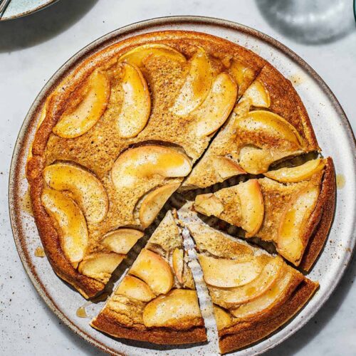 Baked apple pancake upside down on a large plate with four triangles cut.