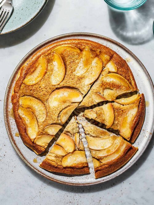Baked apple pancake upside down on a large plate with four triangles cut.