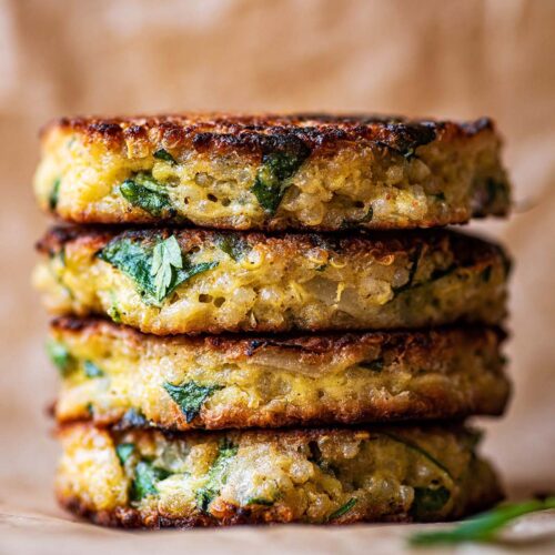 A stack of four quinoa patties on baking paper.