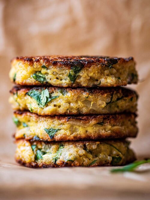 A stack of four quinoa patties on baking paper.