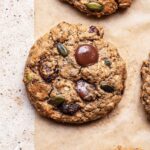 Close up of cookies with seeds and chocolate chunks on parchment paper.