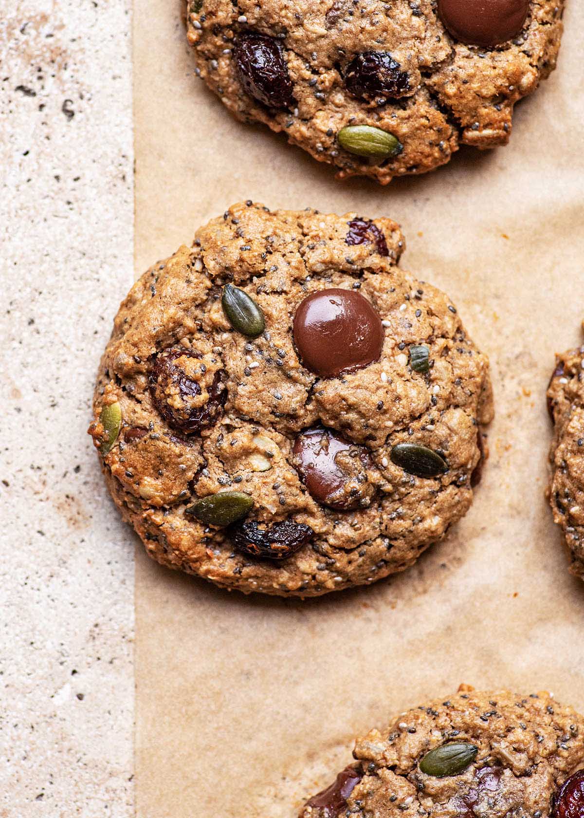 Close up of cookies with seeds and chocolate chunks on parchment paper.