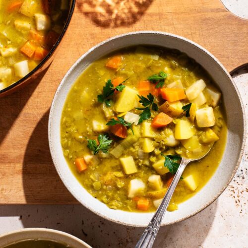 Bowls of pea soup with vegetables on a large wooden cutting board.