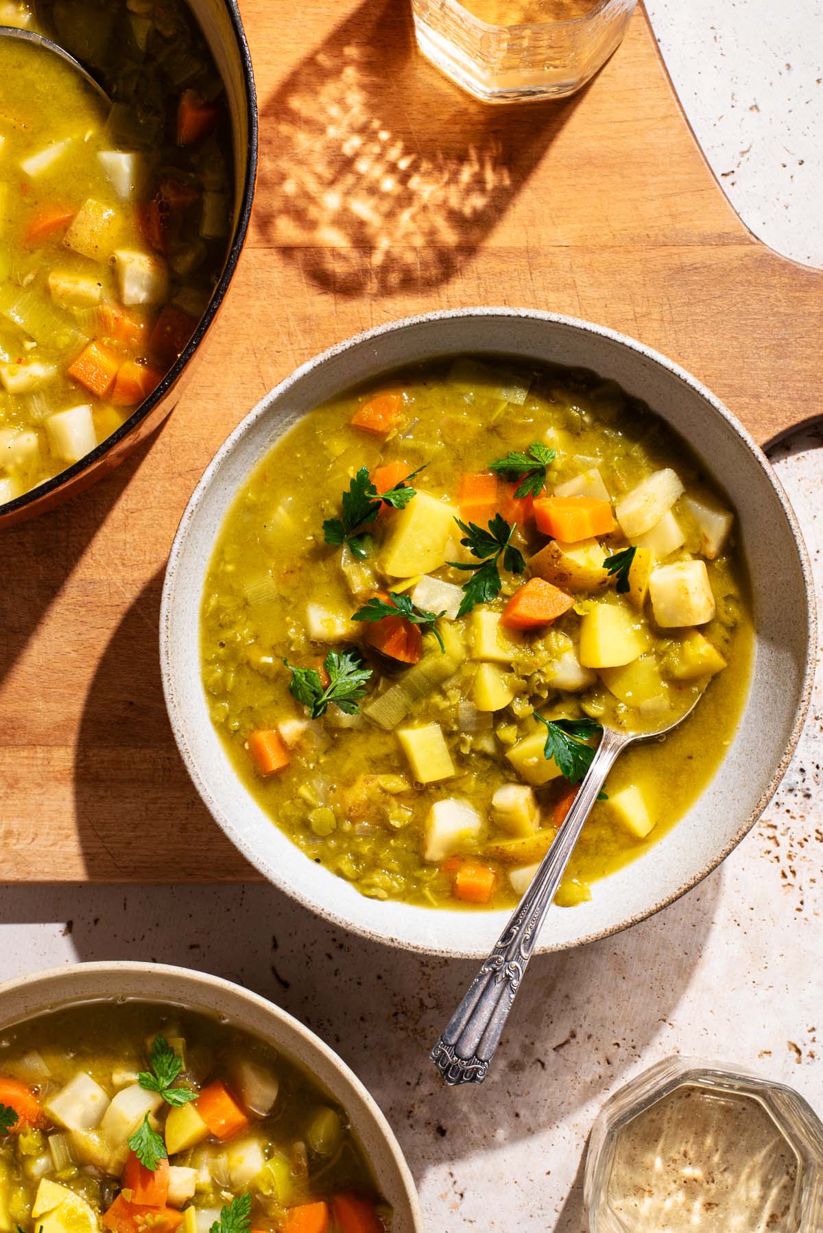 Bowls of pea soup with vegetables on a large wooden cutting board.