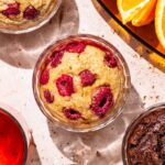 Four glass ramekins with a muffin-like baked batter in them, the central one with raspberries.