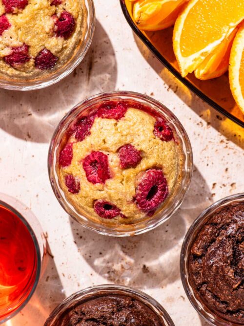 Four glass ramekins with a muffin-like baked batter in them, the central one with raspberries.