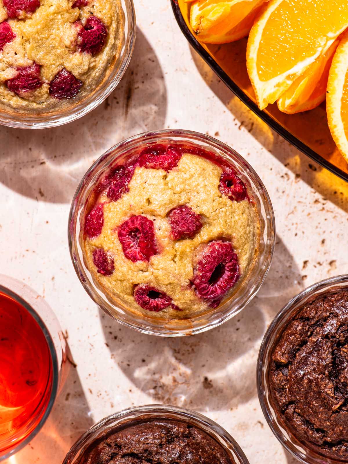 Four glass ramekins with a muffin-like baked batter in them, the central one with raspberries.
