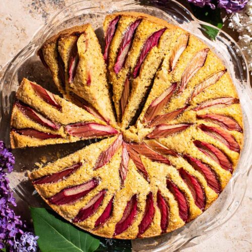 A rhubarb-topped cake with three slices cut, each on a slight angle.
