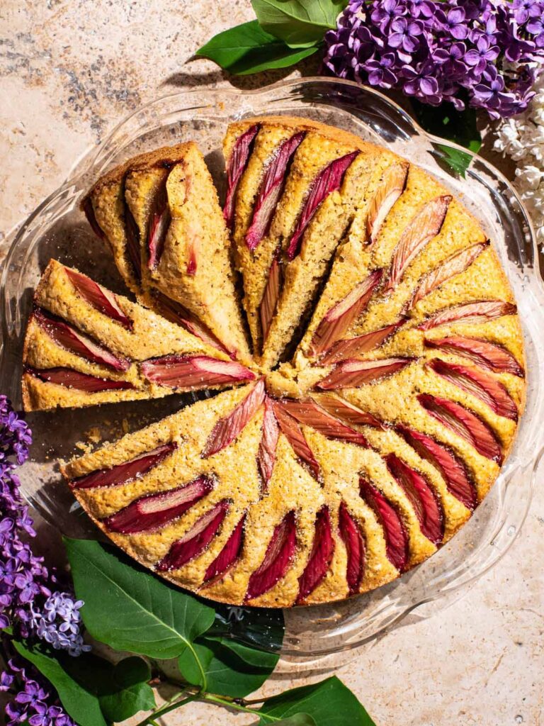 A rhubarb-topped cake with three slices cut, each on a slight angle.