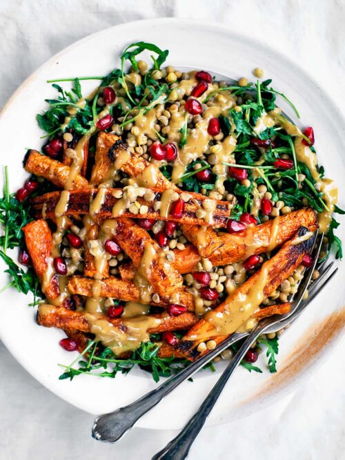 Serving plate with greens, roasted carrots, lentils, and a creamy sauce drizzled on top.