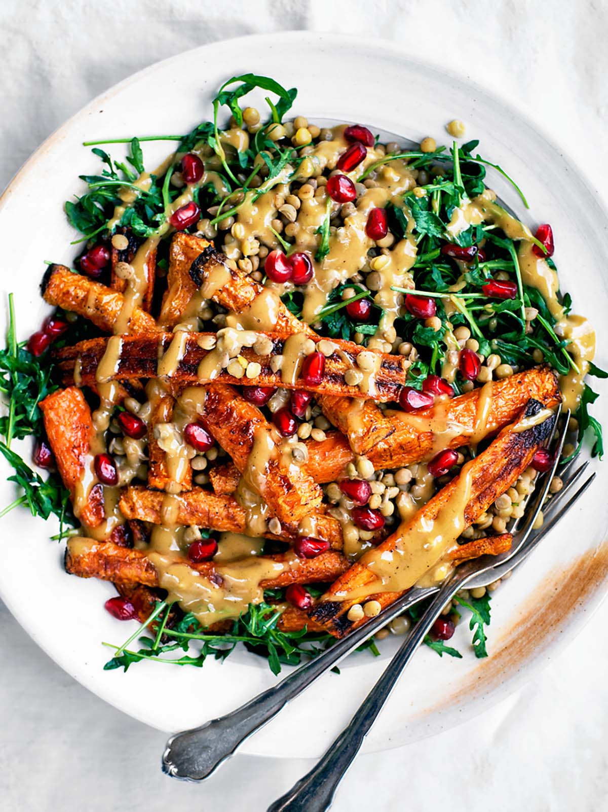 Serving plate with greens, roasted carrots, lentils, and a creamy sauce drizzled on top.