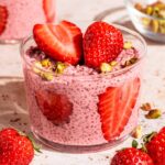 Two jars of pink chia pudding with sliced and halved strawberries.