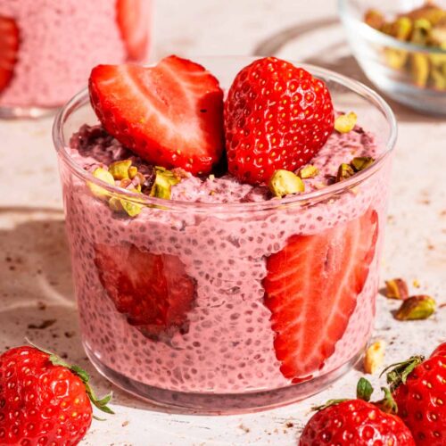 Two jars of pink chia pudding with sliced and halved strawberries.