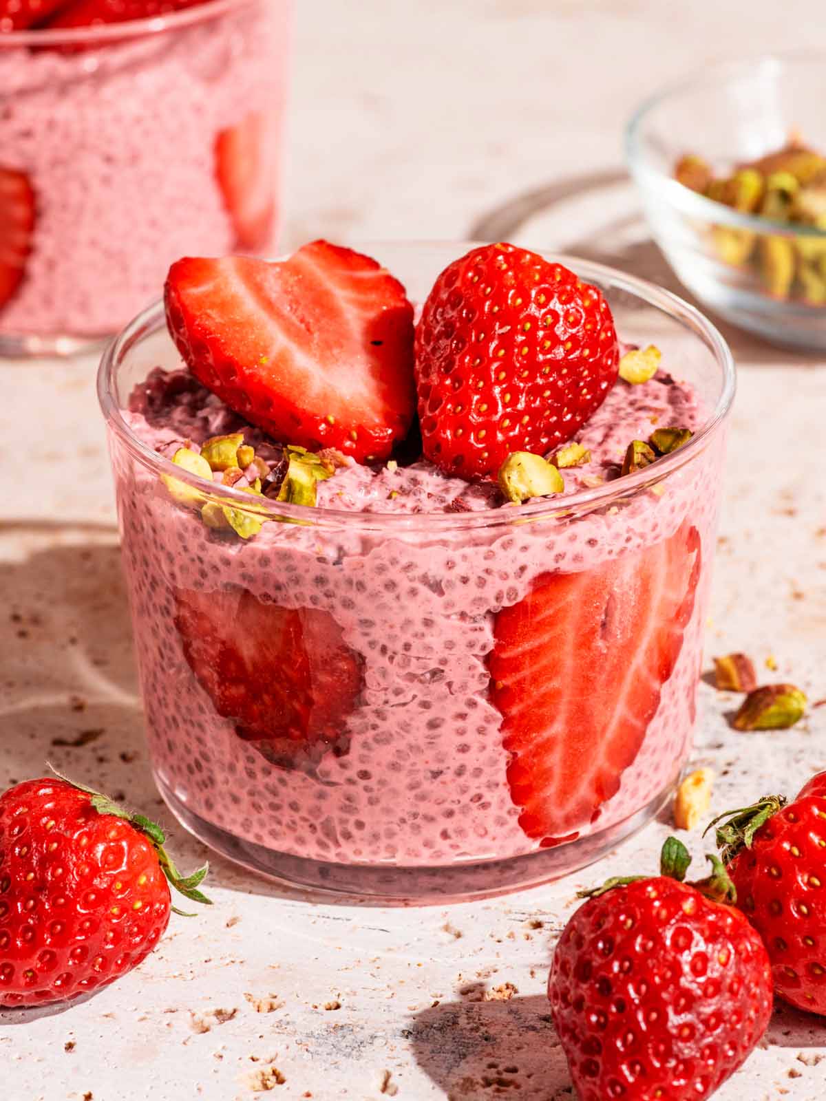 Two jars of pink chia pudding with sliced and halved strawberries.