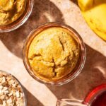 Two servings of baked oats in glass dishes with banana, tea, and rolled oats around.