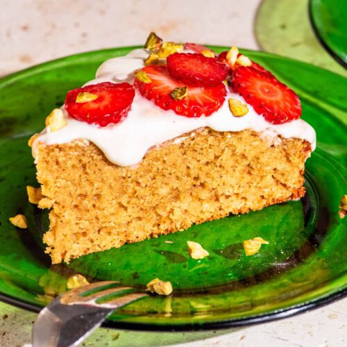 A slice of cake on a green glass plate, topped with frosting and sliced strawberries.