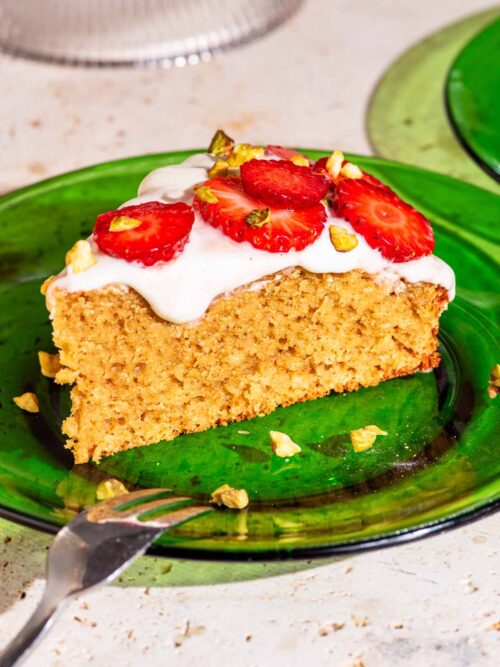 A slice of cake on a green glass plate, topped with frosting and sliced strawberries.