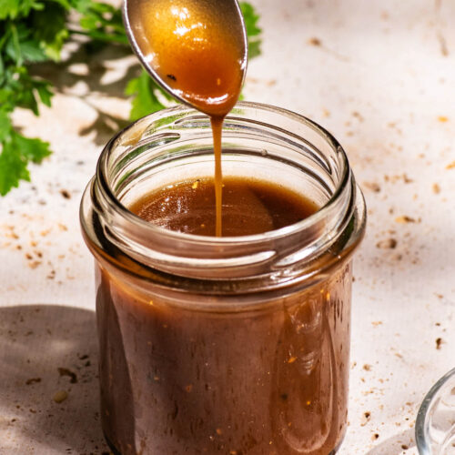 Dark salad dressing in a small glass jar, being drizzled from a spoon back into the jar.