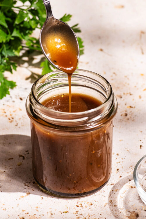 Dark salad dressing in a small glass jar, being drizzled from a spoon back into the jar.