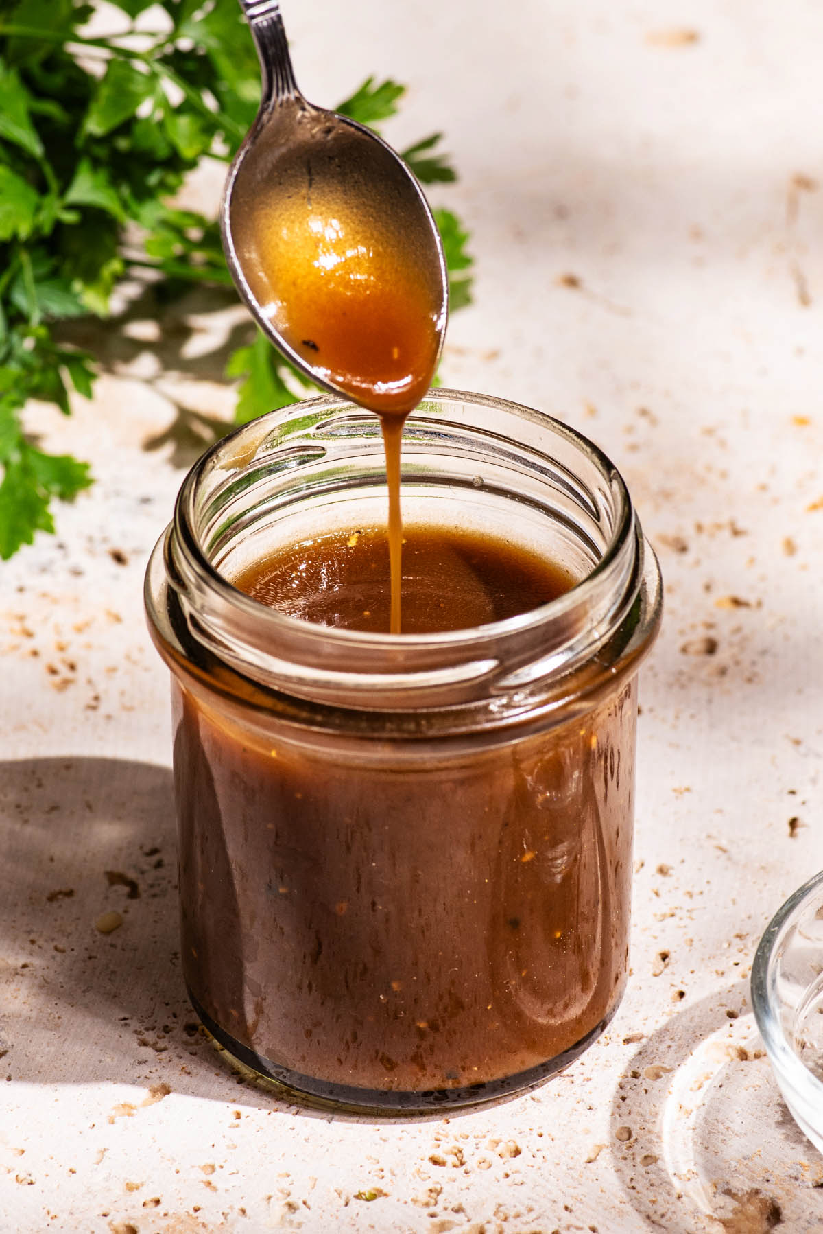 Dark salad dressing in a small glass jar, being drizzled from a spoon back into the jar.