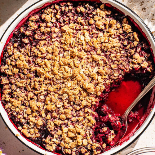 Round baking dish with a dark berry crisp, one serving removes.