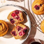 Two blackberry muffins on a plate, one halved, with more on a wire rack.