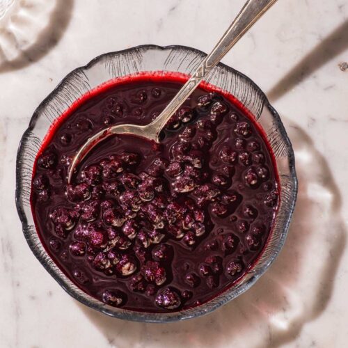 Blueberry sauce in a glass bowl with a spoon.