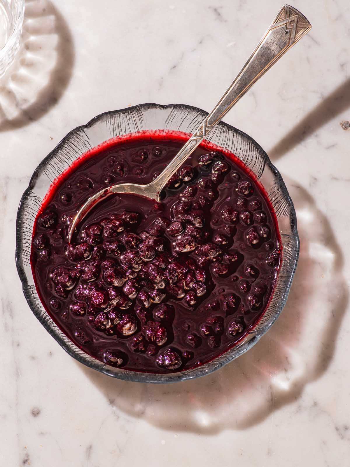 Blueberry sauce in a glass bowl with a spoon.