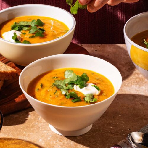 Smooth orange soup in bowls topped with fresh coriander and yogurt.