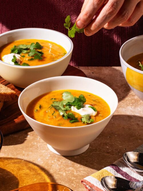 Smooth orange soup in bowls topped with fresh coriander and yogurt.