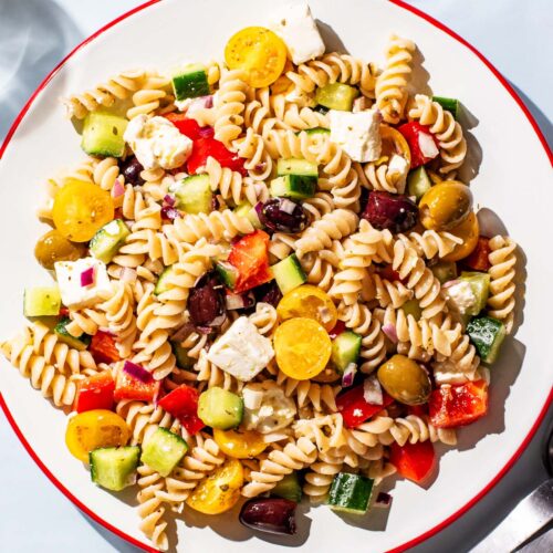 Pasta salad with olives, tomatoes, cucumber, and feta on a large serving plate.