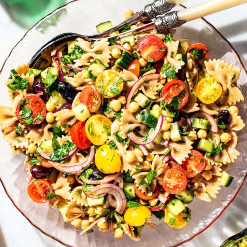Glass serving bowl filled with pasta salad with vegetables and chickpeas.