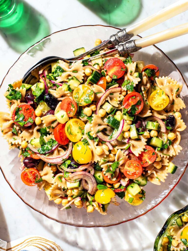 Glass serving bowl filled with pasta salad with vegetables and chickpeas.