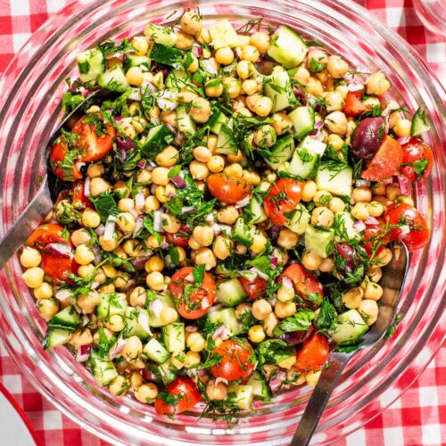 A serving bowl of chickpea vegetable salad on a gingham cloth.