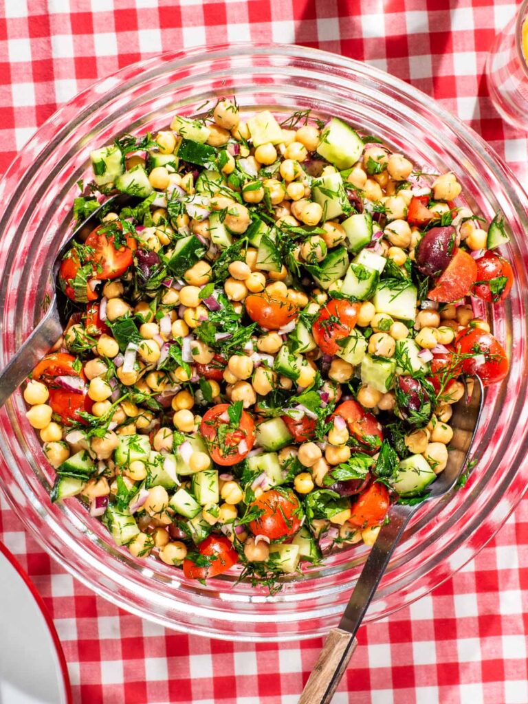 A serving bowl of chickpea vegetable salad on a gingham cloth.