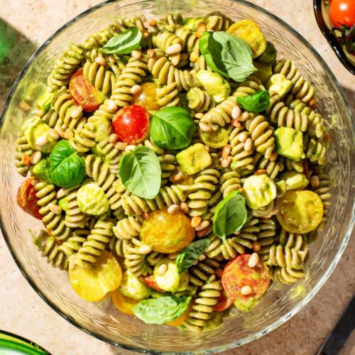 A bowl of pasta salad with a light green dressing, cherry tomatoes, and basil leaves.