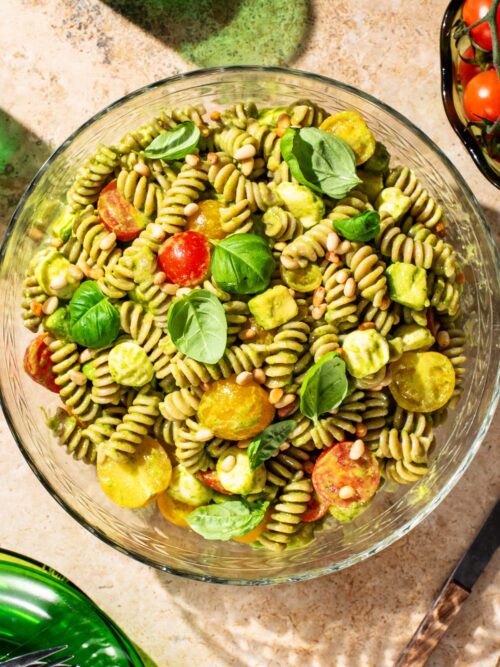A bowl of pasta salad with a light green dressing, cherry tomatoes, and basil leaves.
