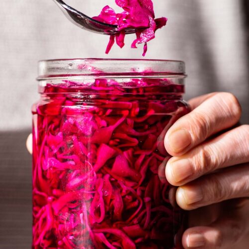 Woman's hands holding a jar of bright pink cabbage, lifting one forkful out of the container.