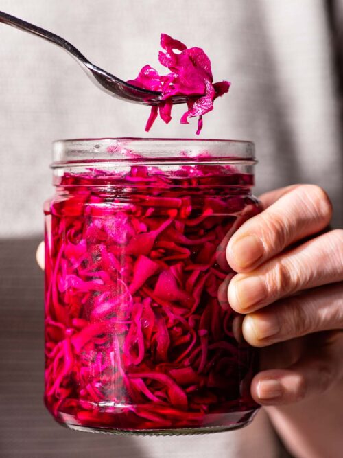 Woman's hands holding a jar of bright pink cabbage, lifting one forkful out of the container.