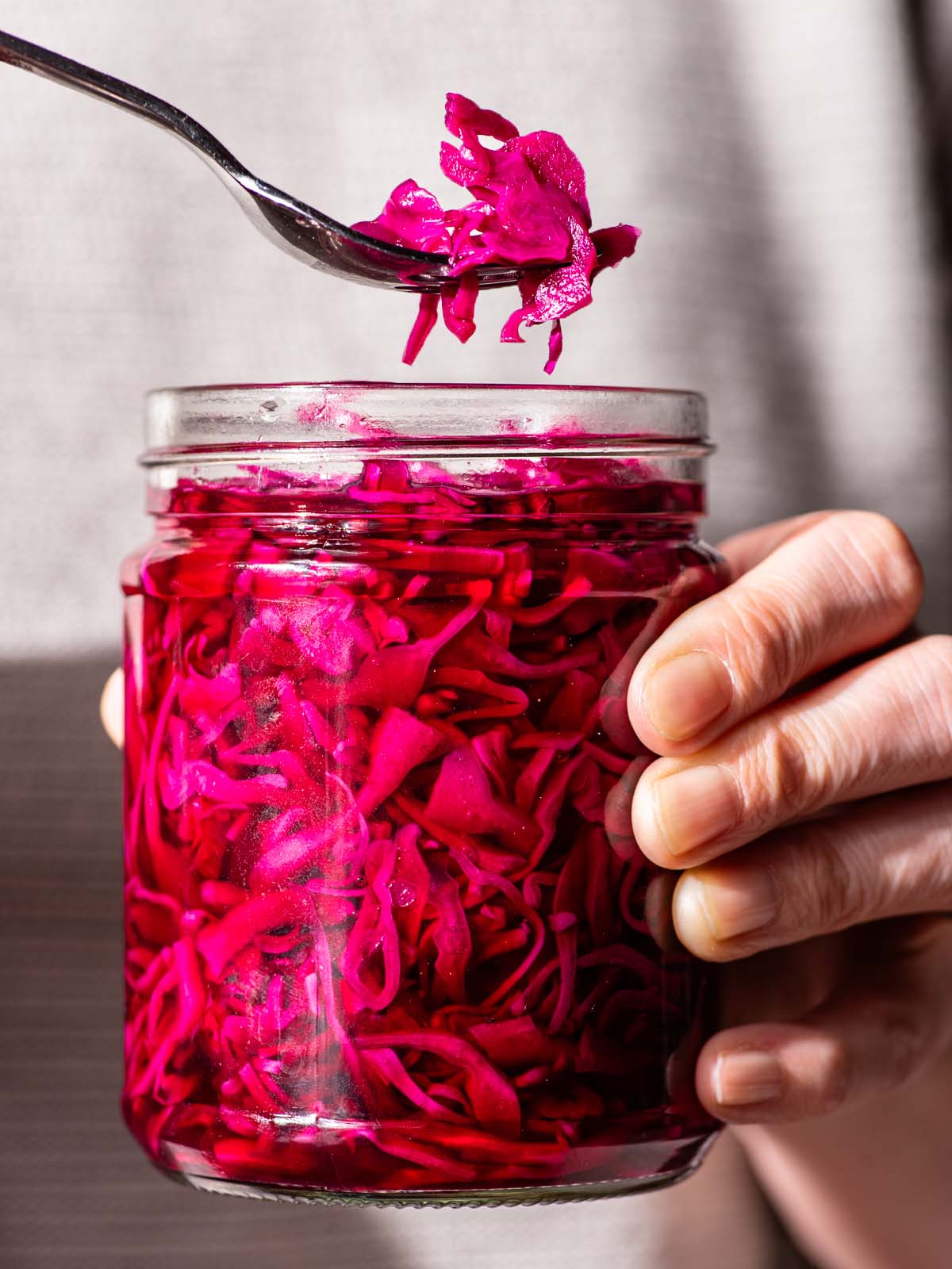 Woman's hands holding a jar of bright pink cabbage, lifting one forkful out of the container.
