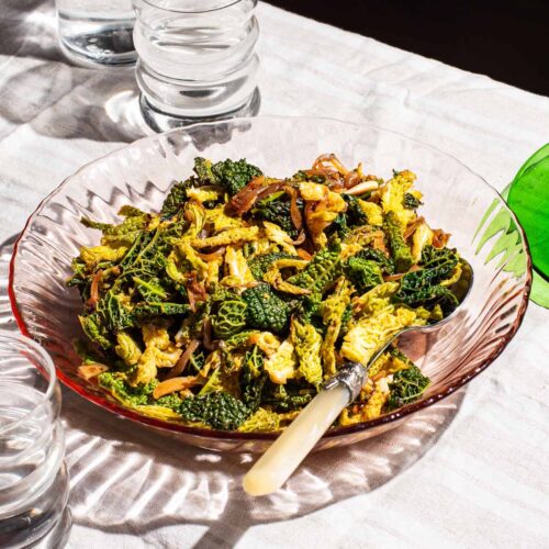 A glass serving bowl of cooked savoy cabbage with onions.