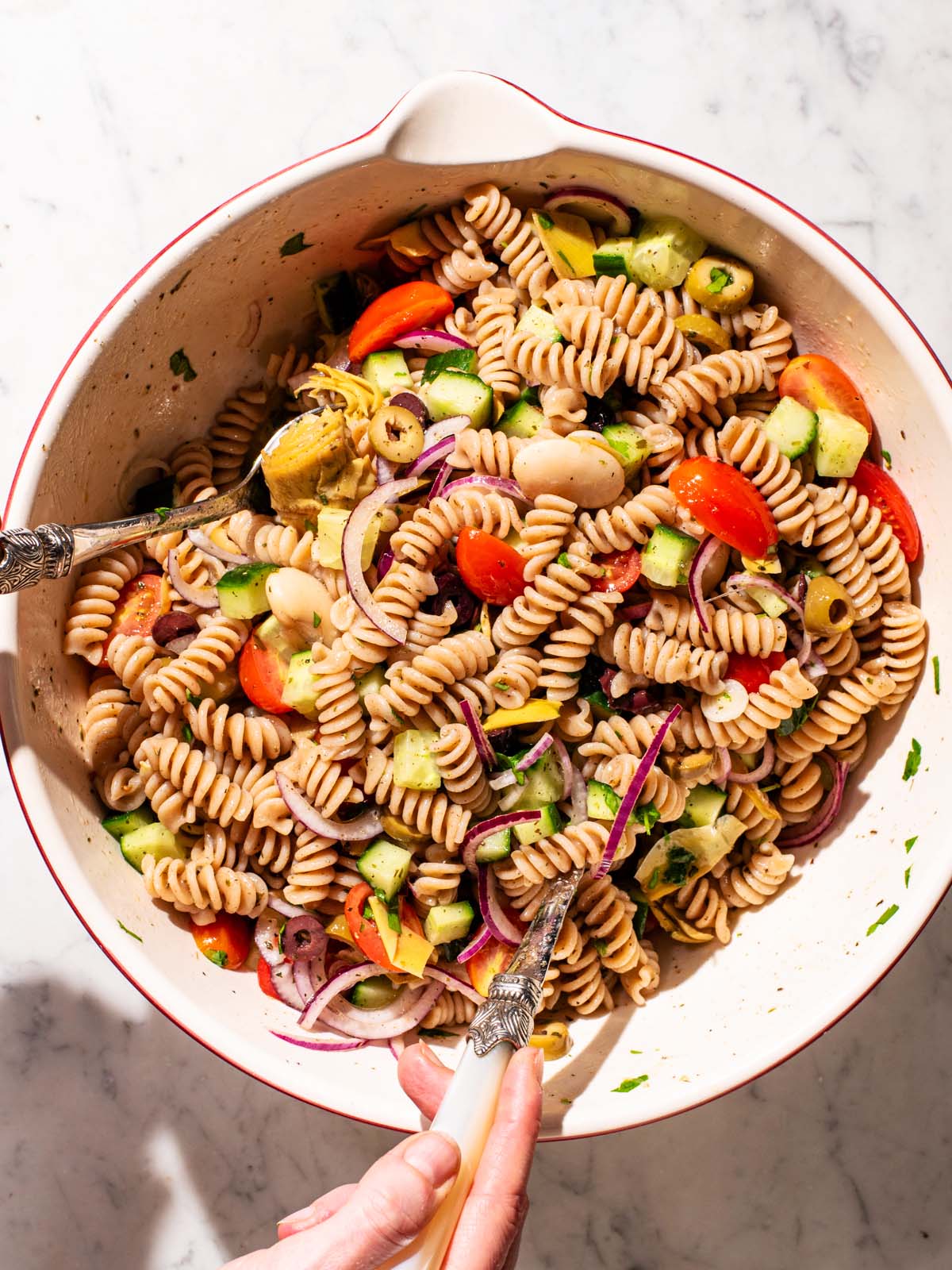 Woman's hands tossing pasta salad in a large mixing bowl.