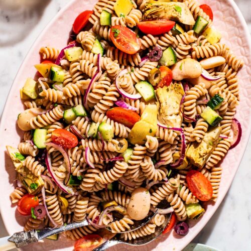 A large light pink platter filled with vegetable pasta salad.
