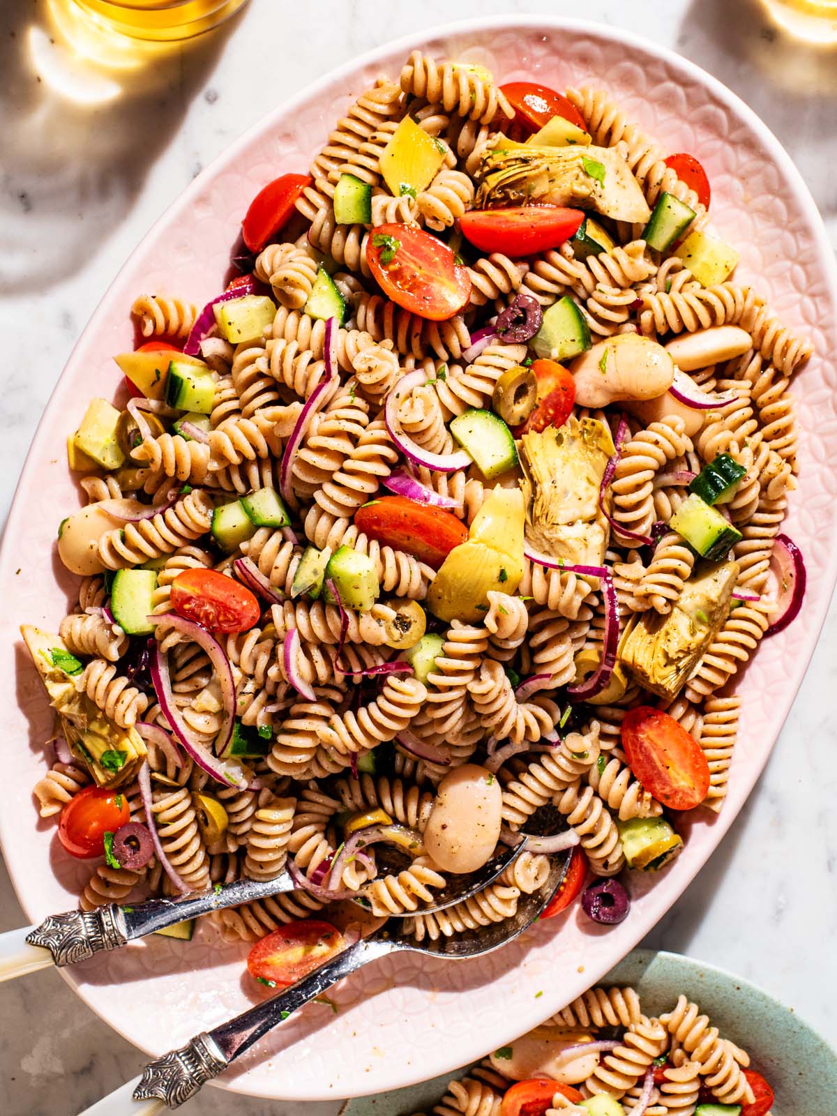 A large light pink platter filled with vegetable pasta salad.