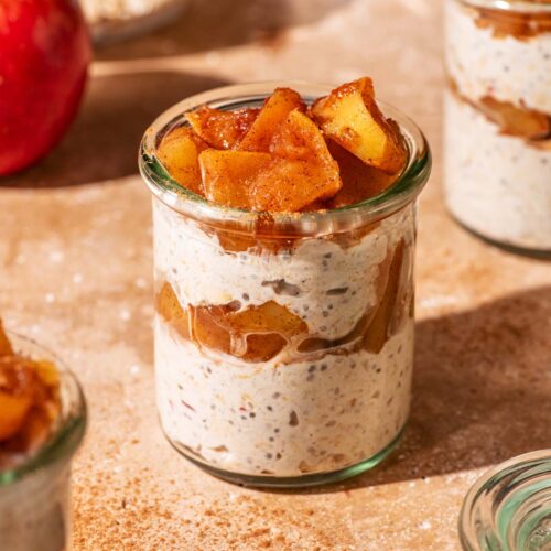 Small glass jars filled with layered overnight oats and cooked apple pieces.