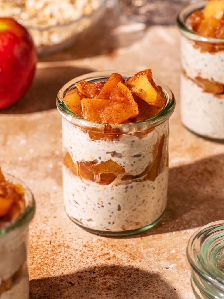 Small glass jars filled with layered overnight oats and cooked apple pieces.